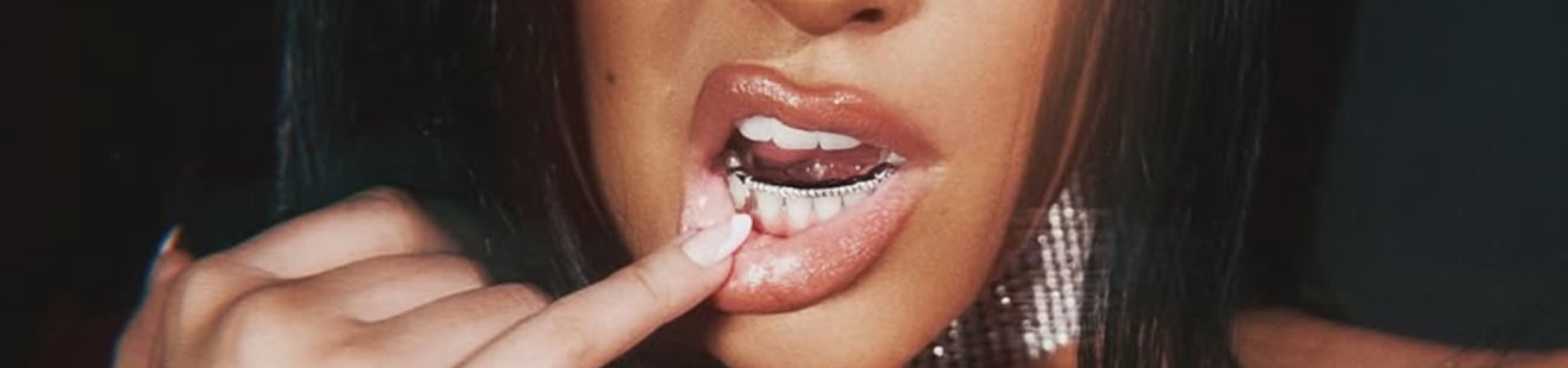 Silver diamond-encrusted bottom grillz shown close-up against glossy lips and statement earrings