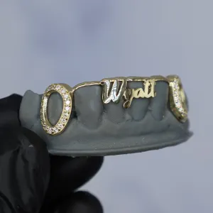 Custom yellow gold bottom grillz with a script name nameplate across the front and pavé diamond oval caps on the outer teeth, shown on a dental cast