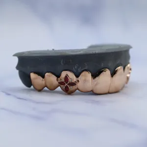 Custom rose gold solid bottom grillz with a marquise ruby floral center motif — four rubies arranged in a flower pattern with diamond accents — shown on a dental cast