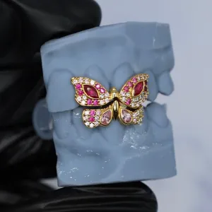 Custom gold butterfly-shaped single-tooth cap set with marquise rubies, round pink diamonds, and white pavé diamonds, shown on a dental cast