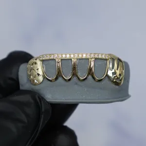 Custom yellow gold open-face bottom grillz with a pavé diamond eternity bar along the top edge, diamond-cut engraved side caps, and an engraved letter cap, shown on a dental mold